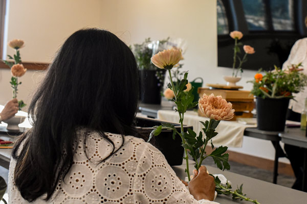 A back of a woman putting together a floral arrangement in class